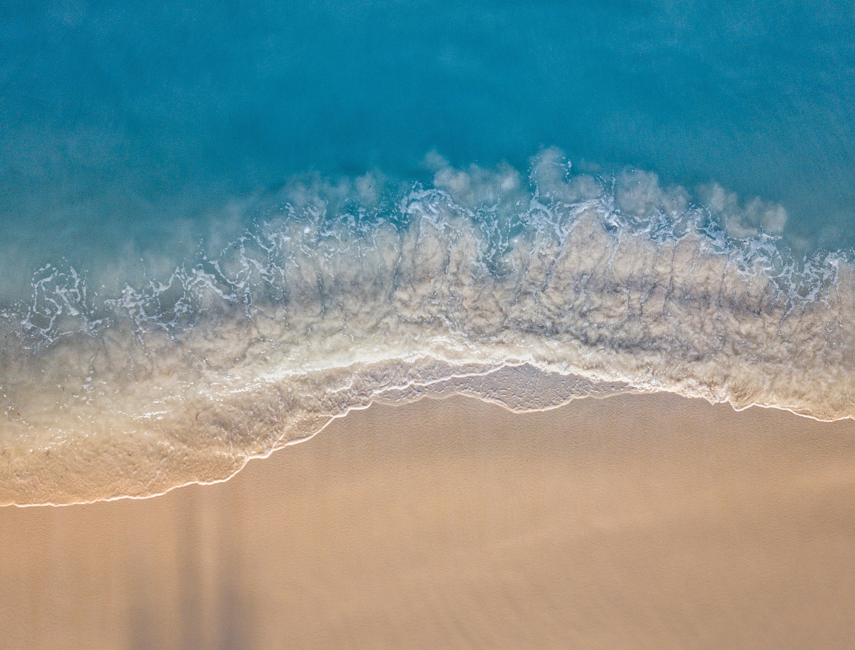 Aerial view of turquoise waves meeting white sand
